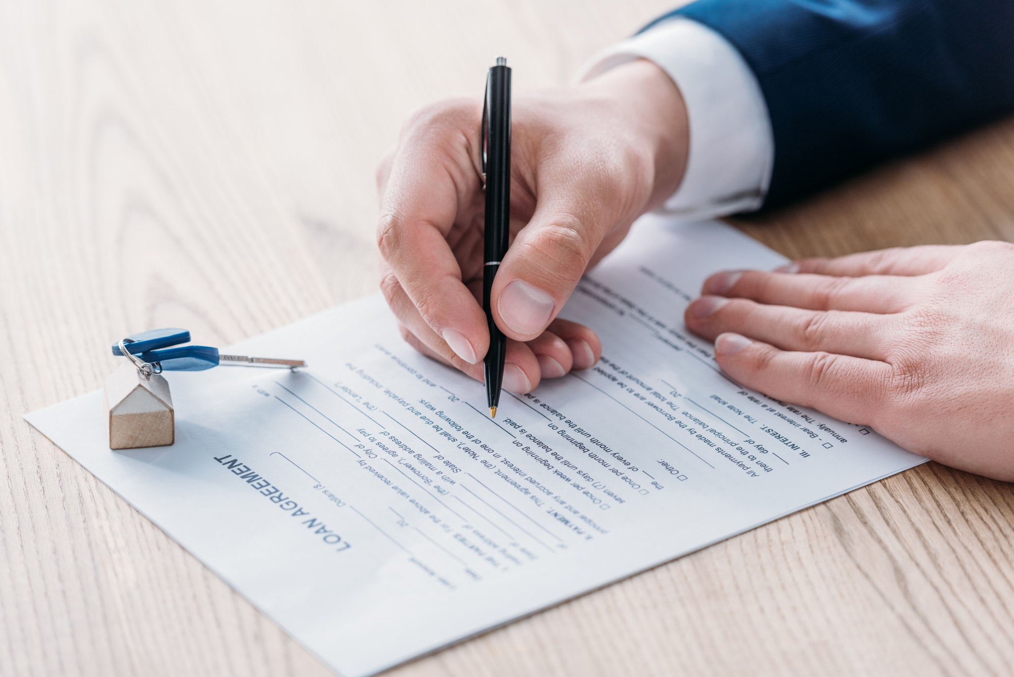 cropped view of realtor writing in loan agreement and car keys on tabletop